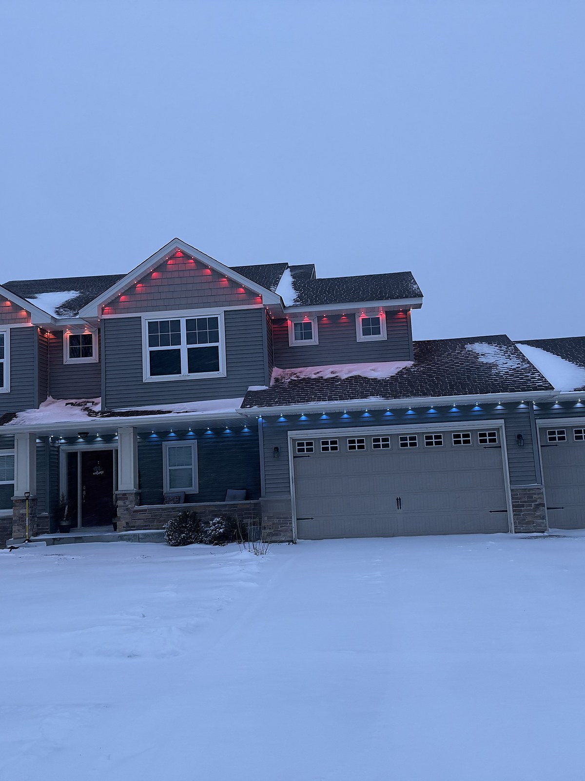 House with red and blue roofline lights on a snowy day